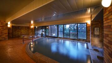 Una piscina interior con suelo de baldosas, paredes de madera y grandes ventanales.