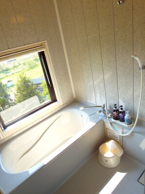 A bathroom with a bathtub, a window, and a showerhead.