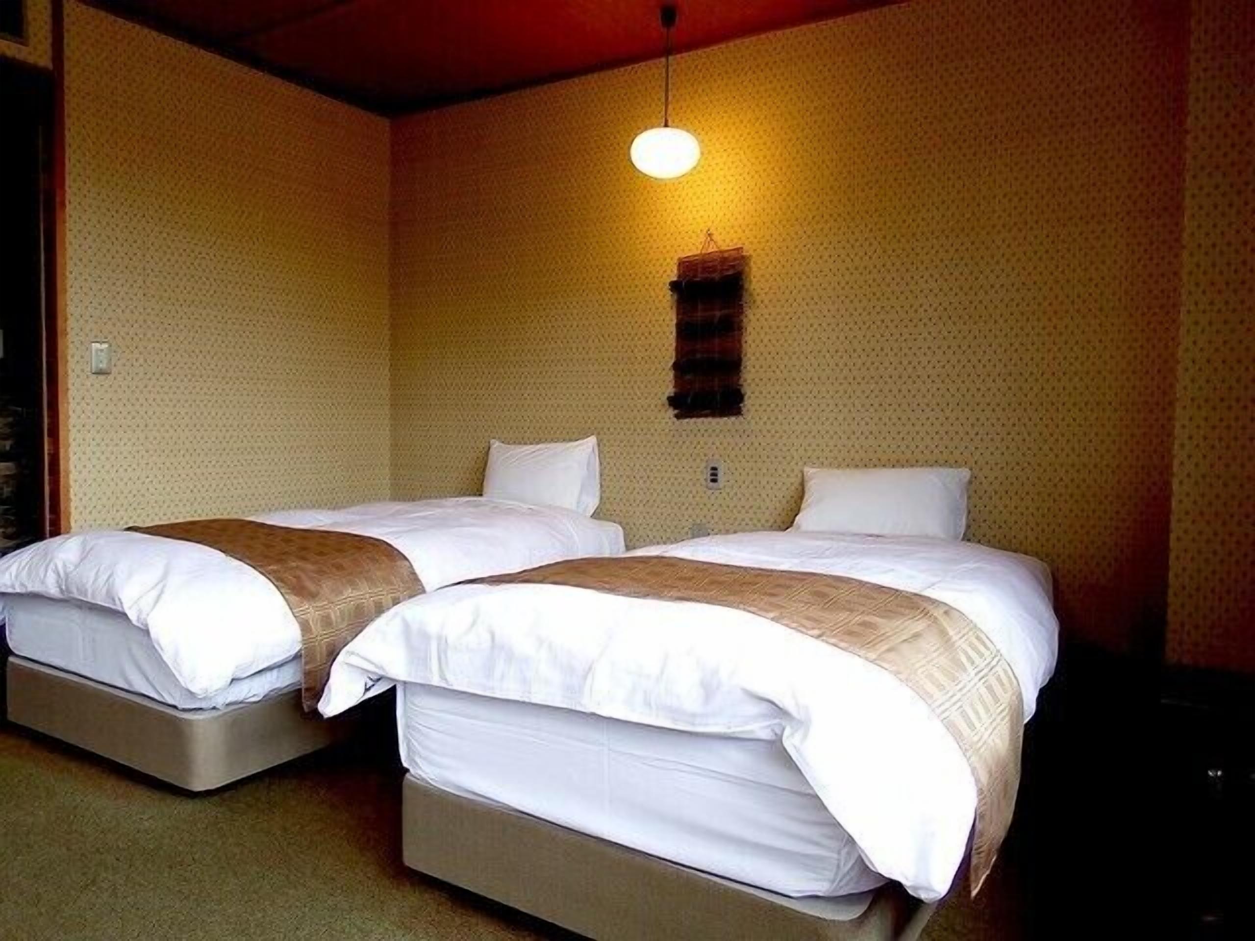 Une chambre avec deux lits, chacun équipé d’un matelas et d’oreillers, d’un luminaire suspendu et d’un mur à texture.