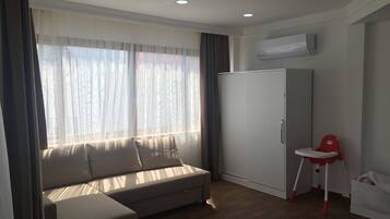 Una habitación moderna con sofá, una mesita, una silla roja, un armario y un equipo de aire acondicionado.
