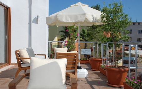 A balcony with wooden chairs and a large umbrella, potted plants, and a sign for the Elegance Hotel.