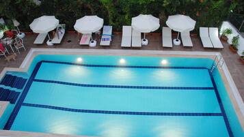 Piscina rectangular con plataforma revestida de azulejos y sillas de descanso con sombrillas.