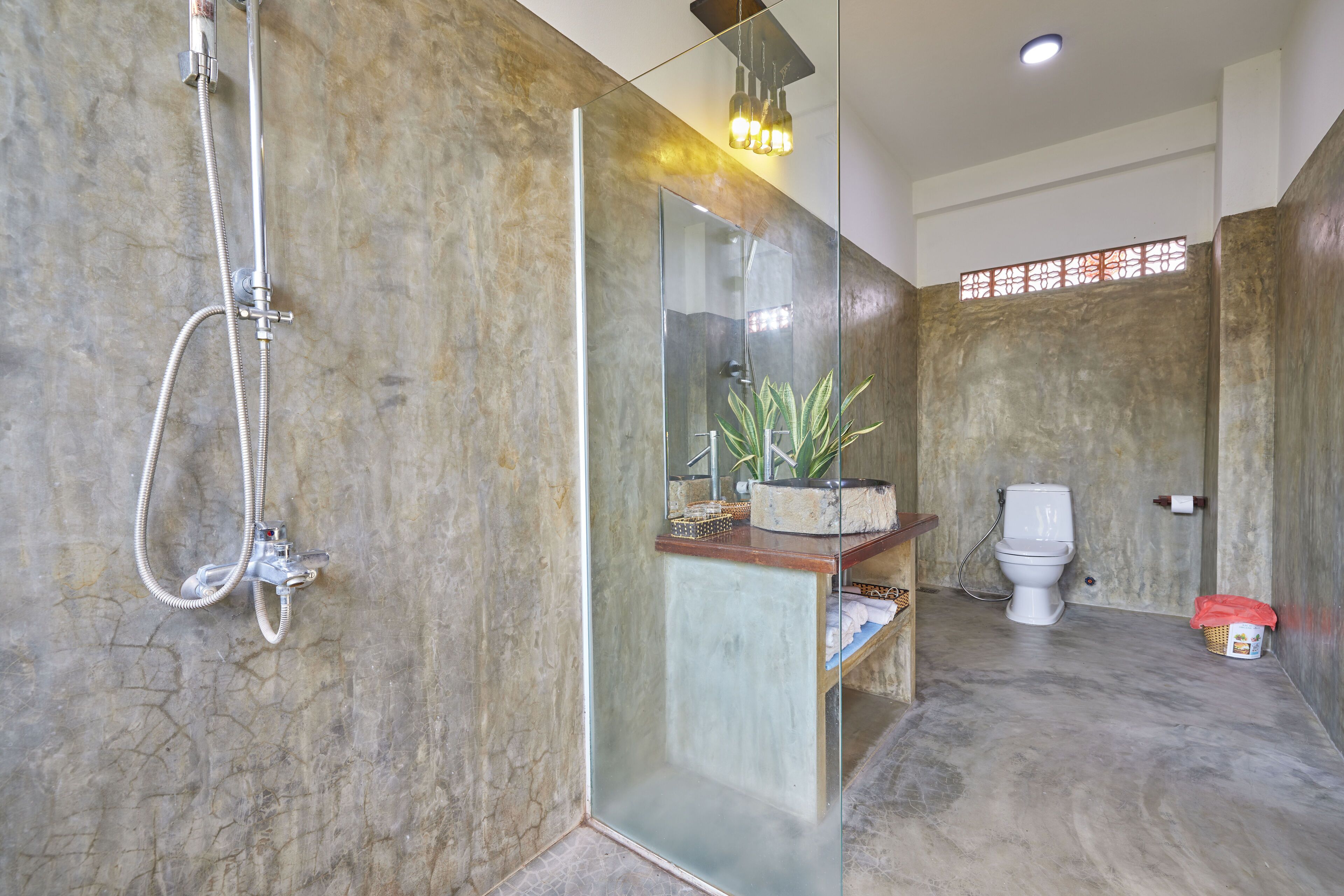 Ein Badezimmer mit Duschkabine aus Glas, Toilette und Waschbecken mit Pflanze auf der Ablagefläche.