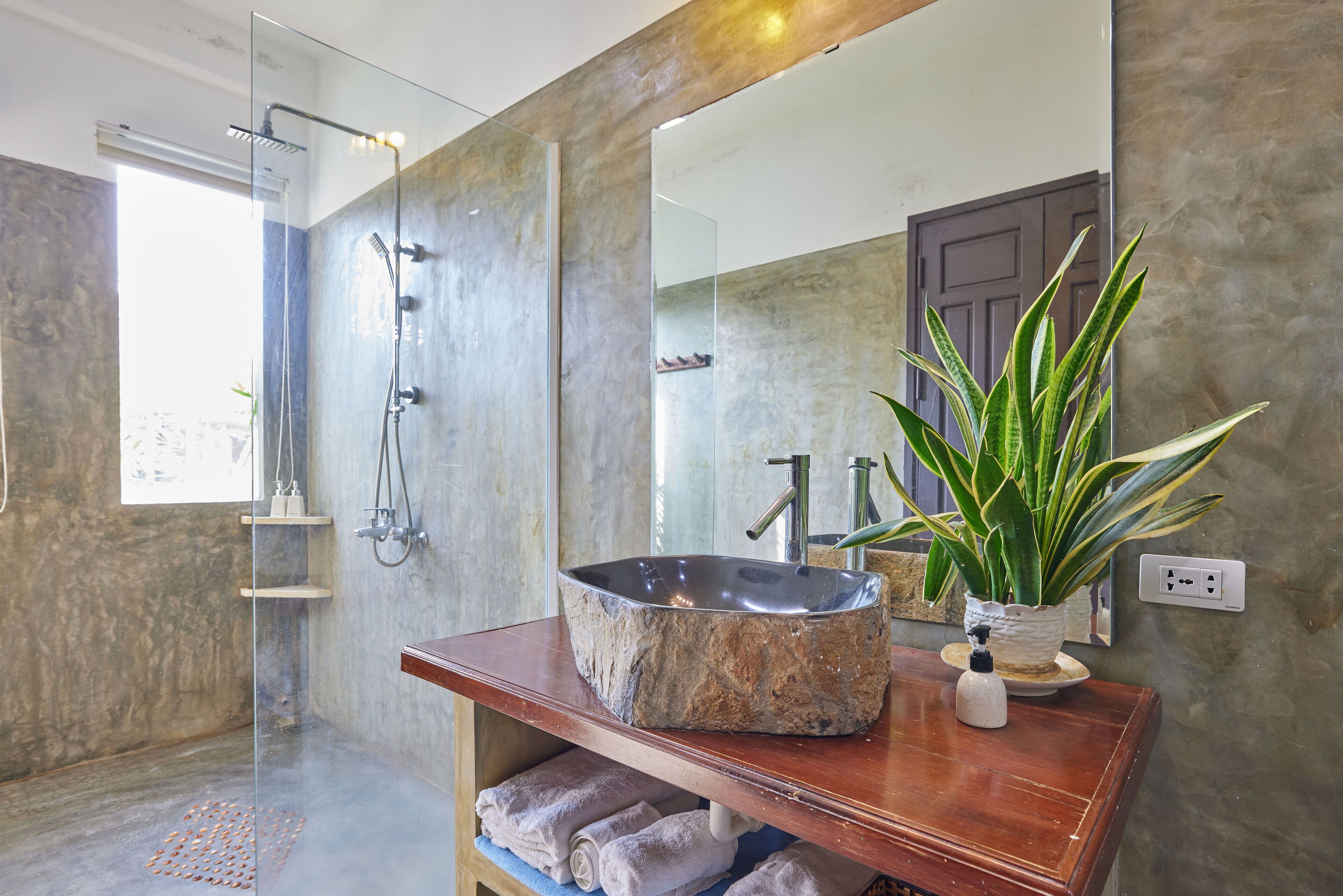A bathroom with a stone sink, a glass shower enclosure, and a potted plant.