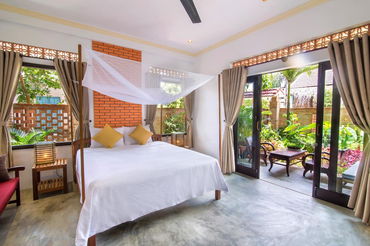 A bedroom with a bed, a small table, and chairs. There is a view of a garden through the glass door.