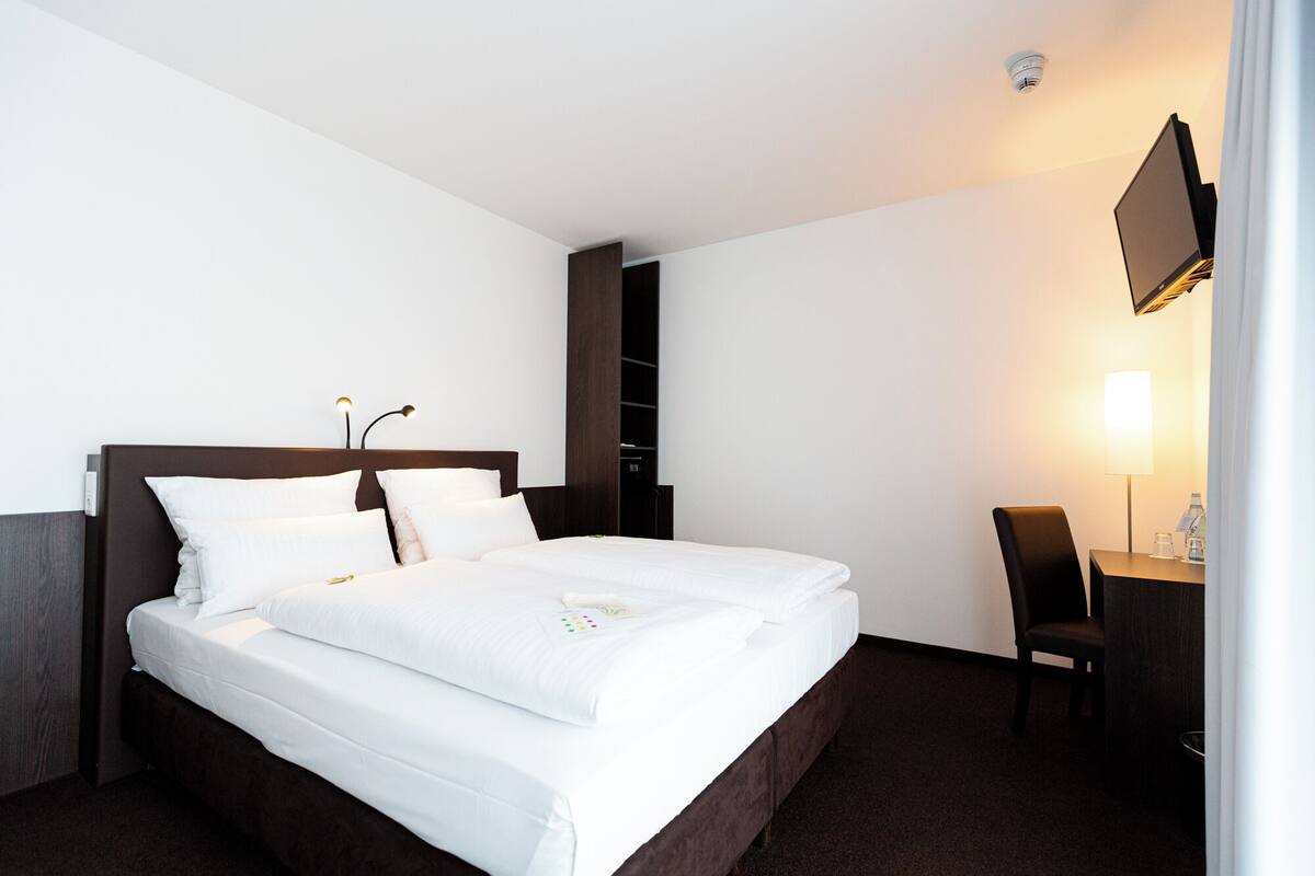 Habitación de hotel con una cama grande, un escritorio con silla, televisor montado en la pared y un armario.