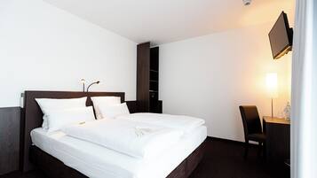 Habitación de hotel con una cama grande, un escritorio con silla, televisor montado en la pared y un armario.