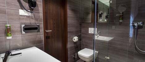 A modern bathroom with a large white sink, a glass-enclosed shower, a toilet, and a hairdryer mounted on the wall.