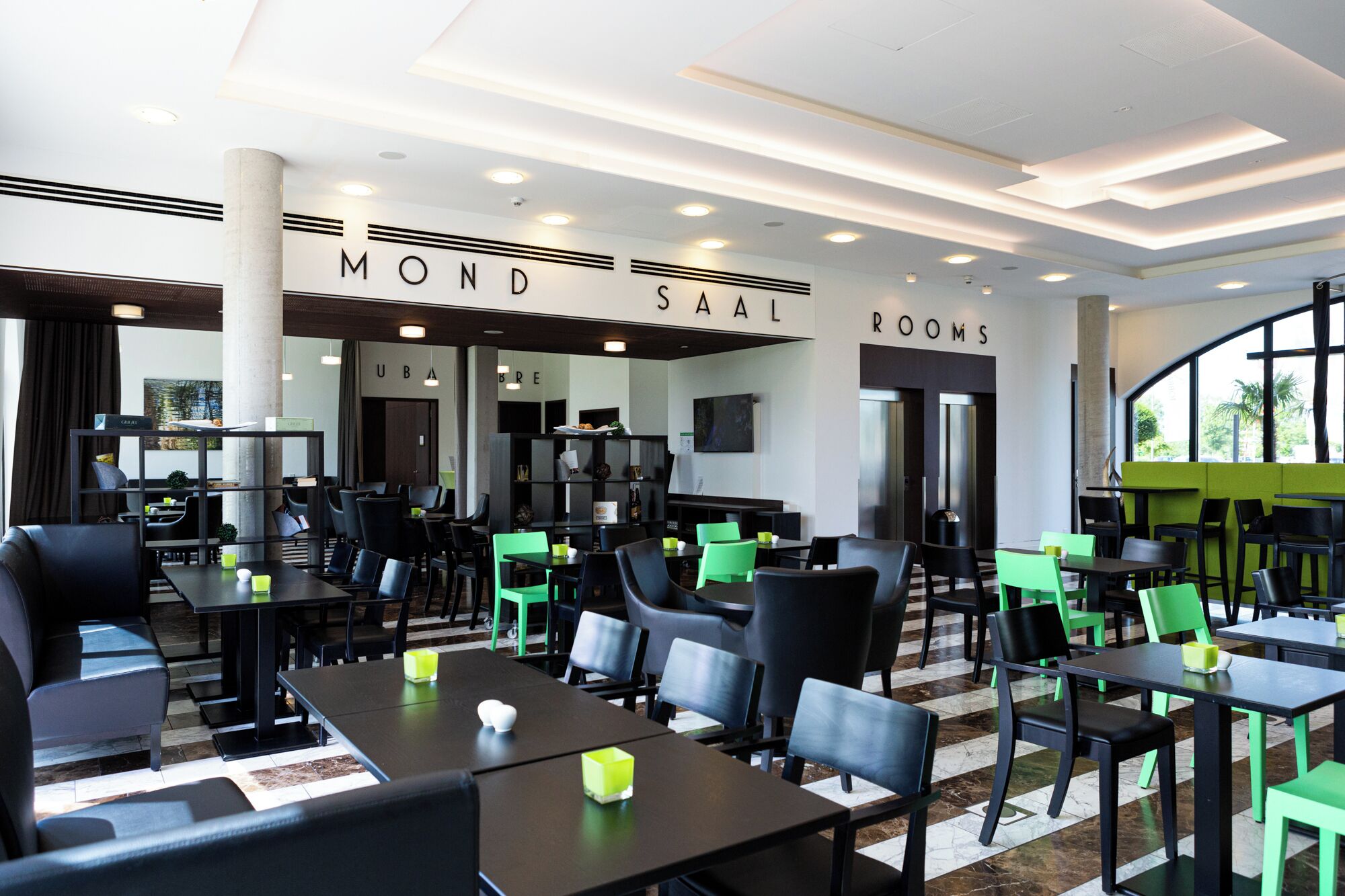 Ein modernes Restaurant mit schwarzen und grünen Stühlen sowie Tischen und einer Decke mit eingelassener Beleuchtung.