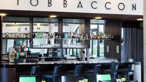 A bar area with a sign reading "TOBBACCON" and shelves stocked with various bottles and glasses. - Hotel Tobbaccon (Bensheim)