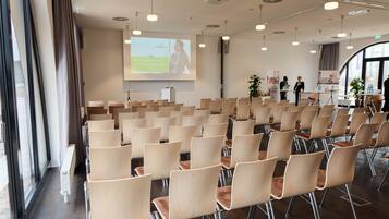 Un salón de conferencias con filas de sillas, una pantalla de proyector y una zona de presentaciones.
