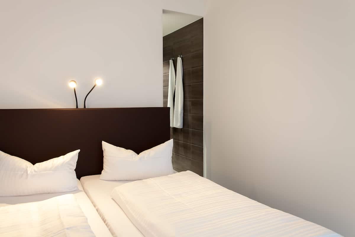 Una habitación de hotel moderna con una cama grande, dos mesitas de noche y un cabecero oscuro.
