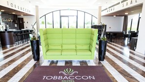 A lobby with a green sofa, a reception desk, and a marble floor. - Hotel Tobbaccon (Bensheim)