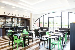 Un restaurante con zona de bar, asientos con sillas verdes y negras, y vista al exterior.