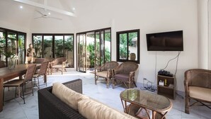 Un amplio salón con un televisor grande, muebles de mimbre y una mesa de comedor.