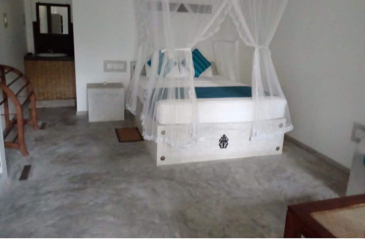 A bedroom with a bed under a canopy, a small bedside table, and a chair.