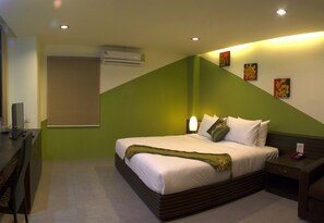 Una habitación de hotel con cama, mesita de noche, lámpara y aire acondicionado instalado en la pared.