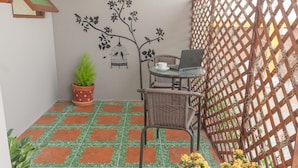 A small balcony with a tiled floor, a wicker chair, a table with a laptop, a potted plant, and a decorative wall mural. - M Y Home Hotel (Chiang Mai)