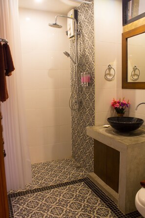 Un baño con piso estampado, un lavamanos tipo cuenco negro, una ducha con cabezal de ducha manual y un espejo con marco de madera.