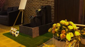 A room with a brick wall, a black piano, a white easel, and a bouquet of yellow flowers. - M Y Home Hotel (Chiang Mai)