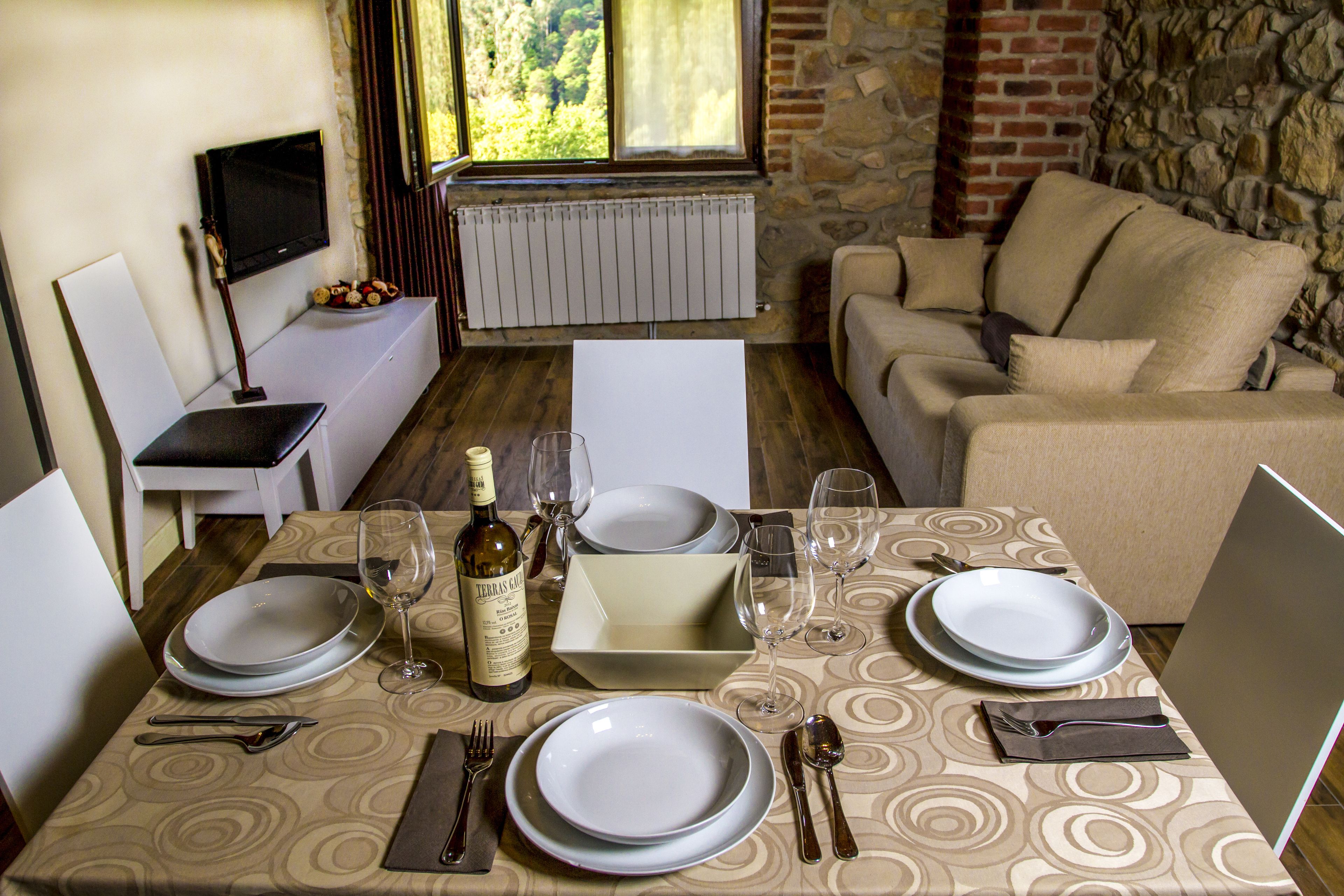 Comedor con una mesa preparada para cuatro personas, con platos, cubiertos y copas de vino.