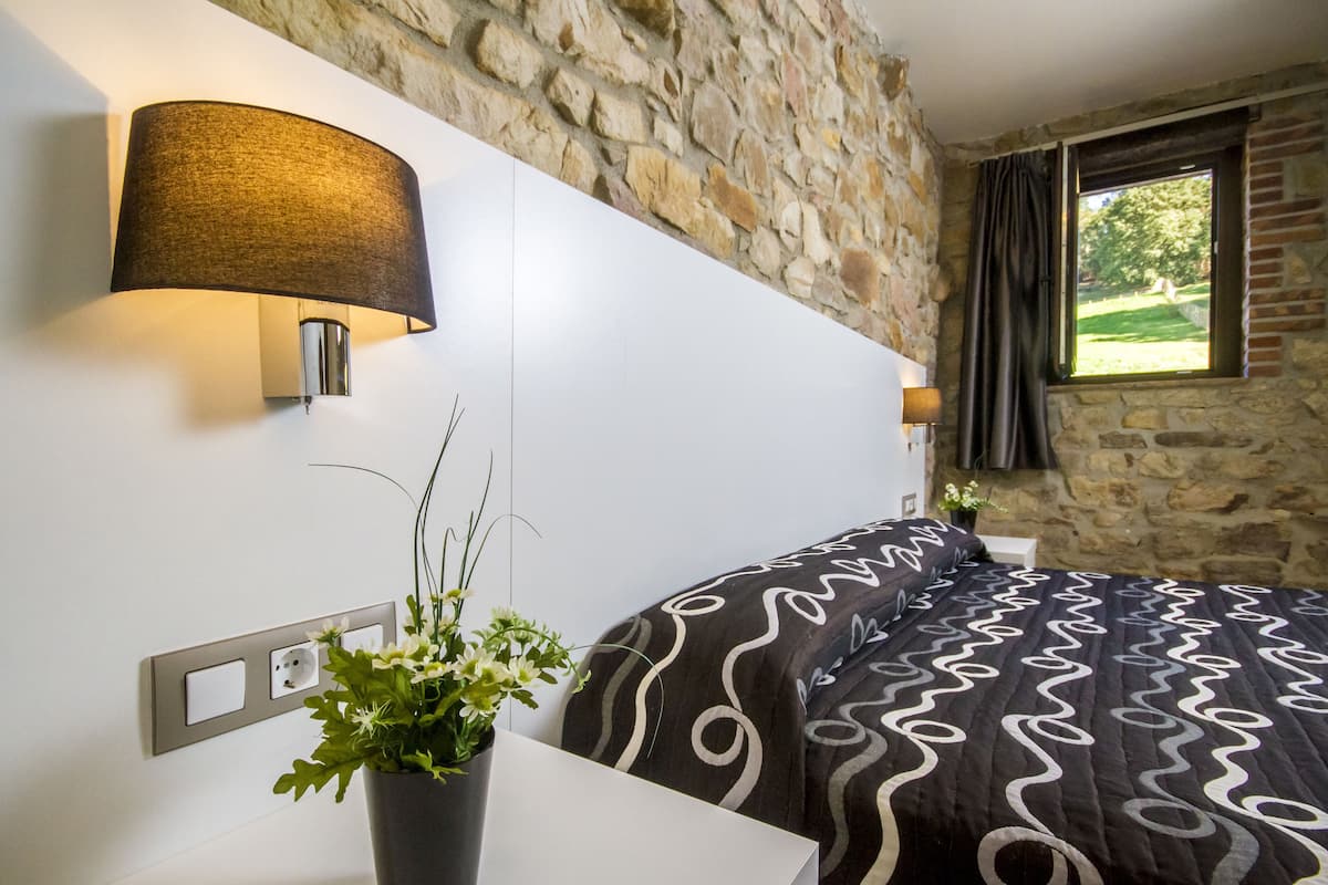 Un dormitorio con pared de piedra, una cama con colcha estampada, una lámpara de pared y una planta en maceta.