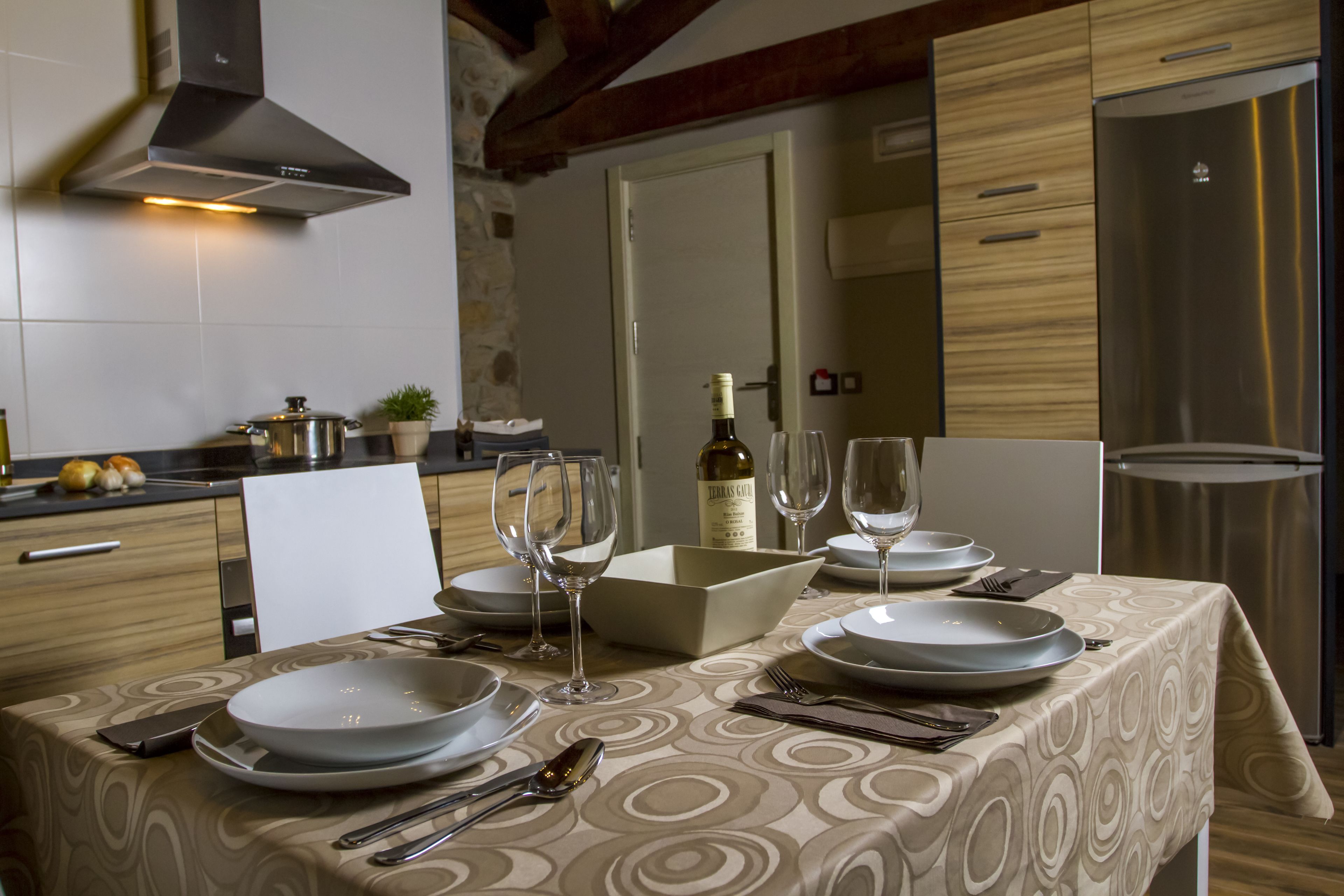 Una mesa lista para comer, con platos, vasos, cubiertos, una botella de vino y un cuenco de fruta.