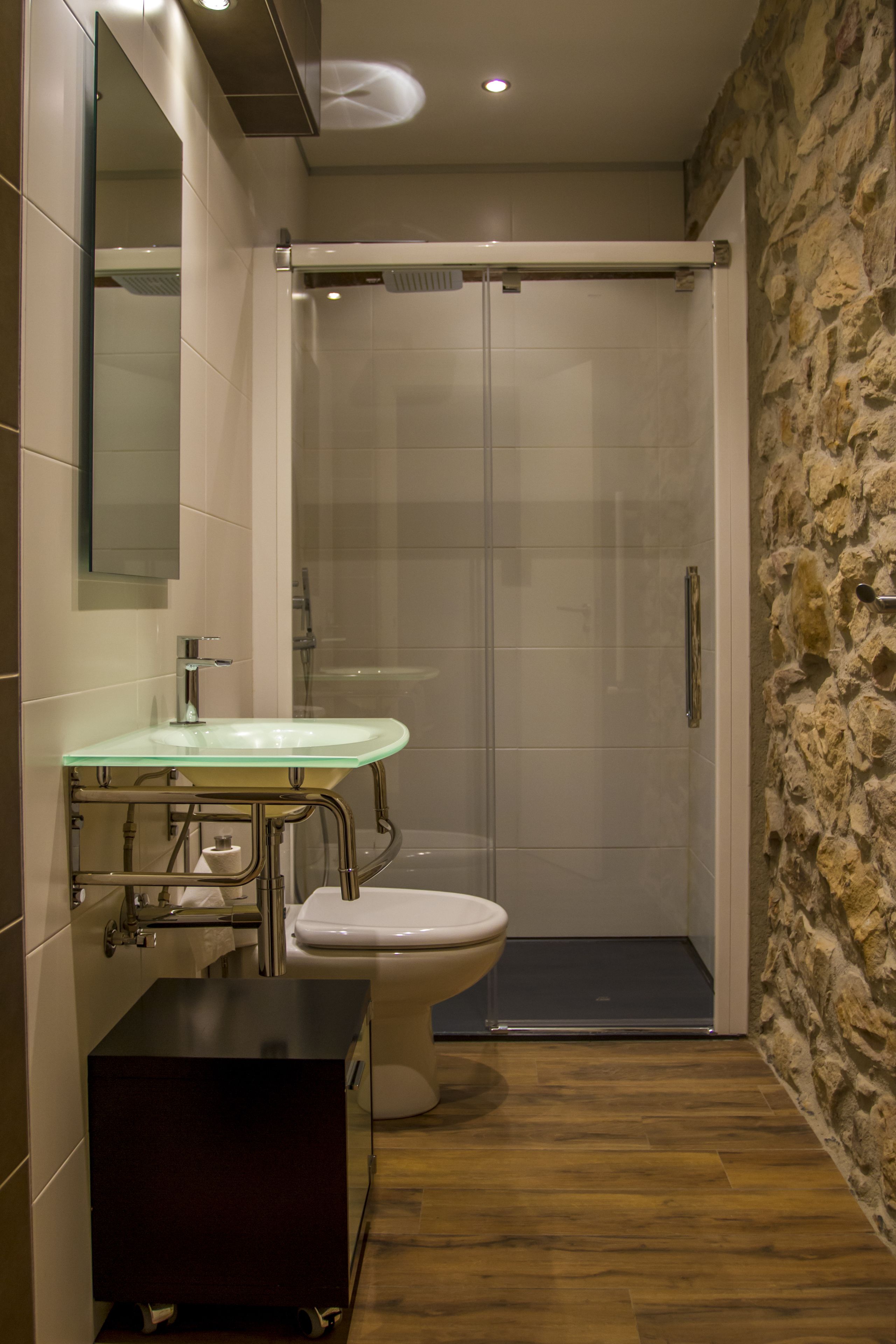 A bathroom with a glass shower enclosure, a glass sink, and a toilet.