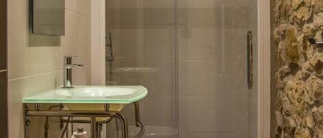 A bathroom with a glass shower enclosure, a glass sink, and a toilet.