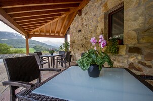 Un patio exterior con mobiliario de mimbre, una mesa de vidrio y una maceta con flores.