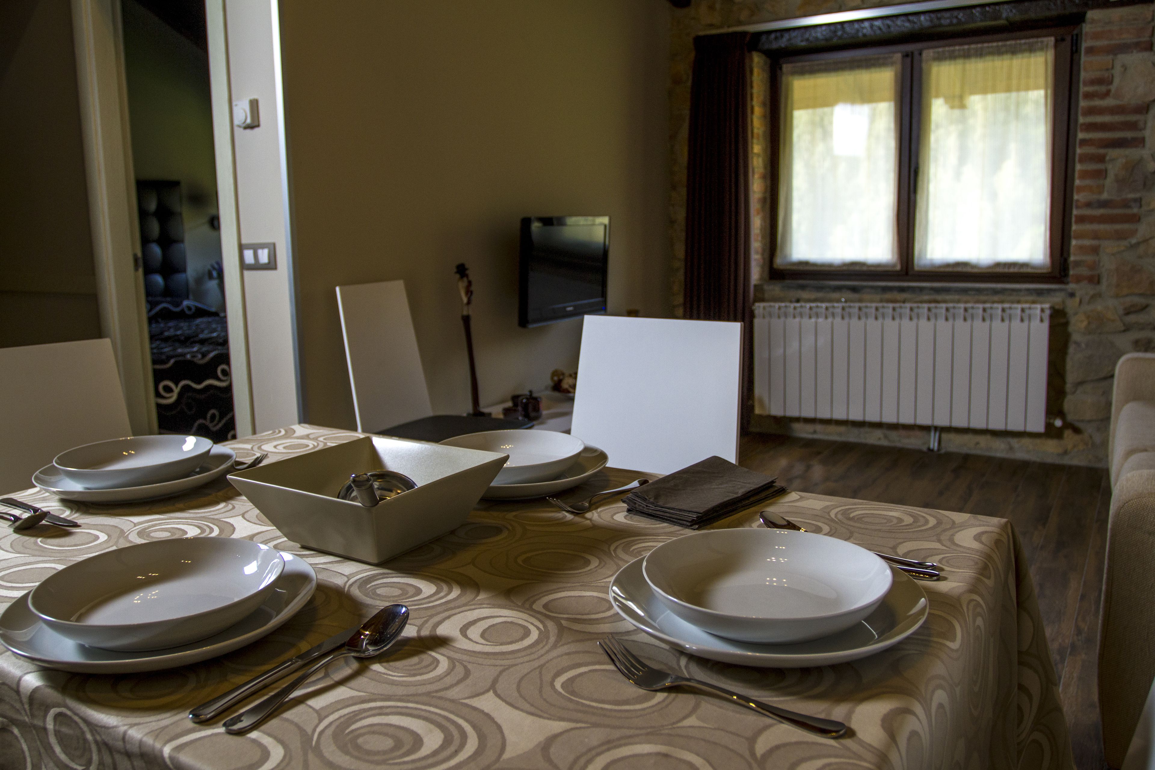 A dining table set with plates, cutlery, and a bowl, in a room with a television, window, and radiator.