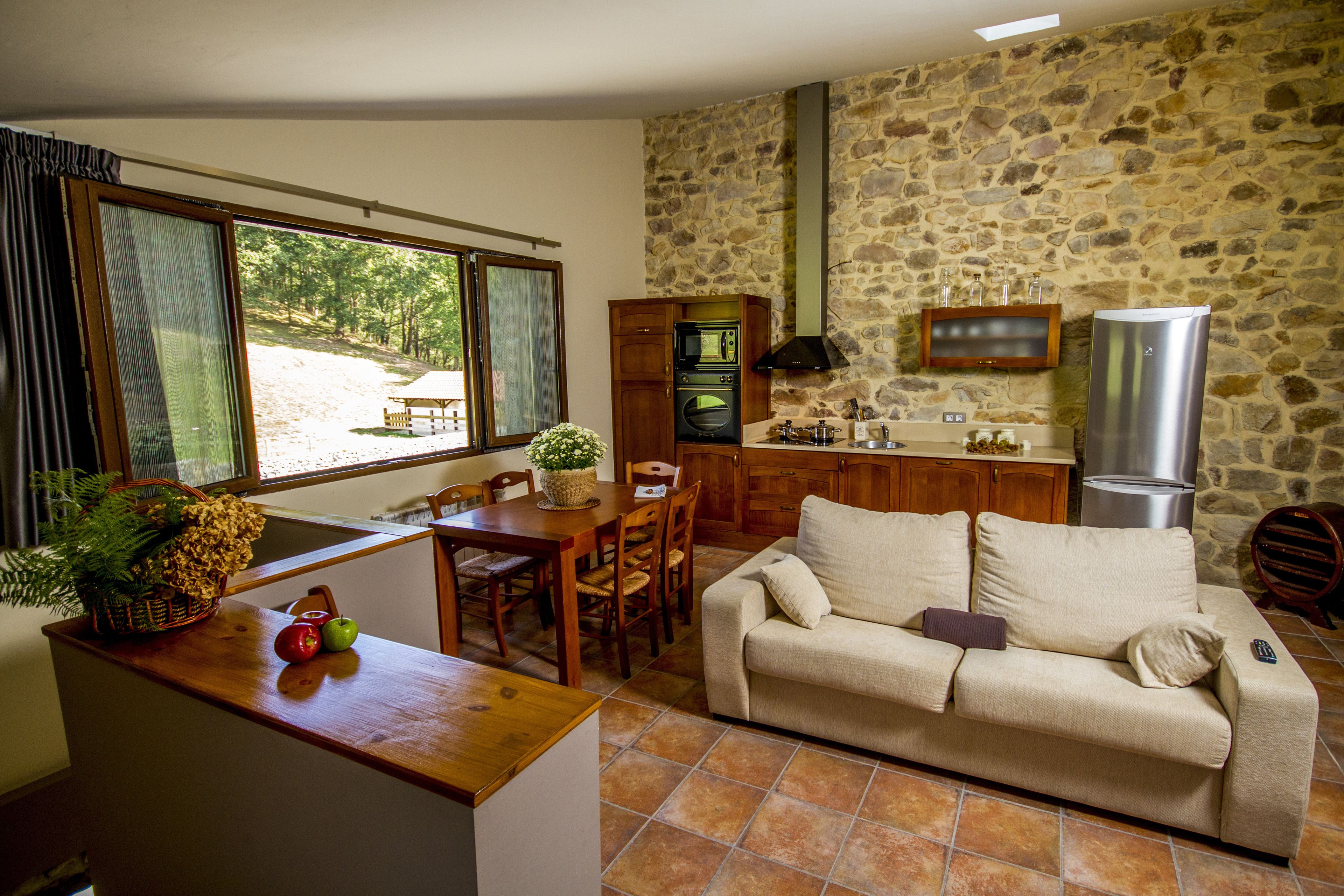 A cozy living area with a wooden dining table, a sofa, and a kitchen with stone walls and modern appliances.