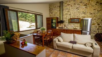 A cozy living area with a wooden dining table, a sofa, and a kitchen with stone walls and modern appliances.