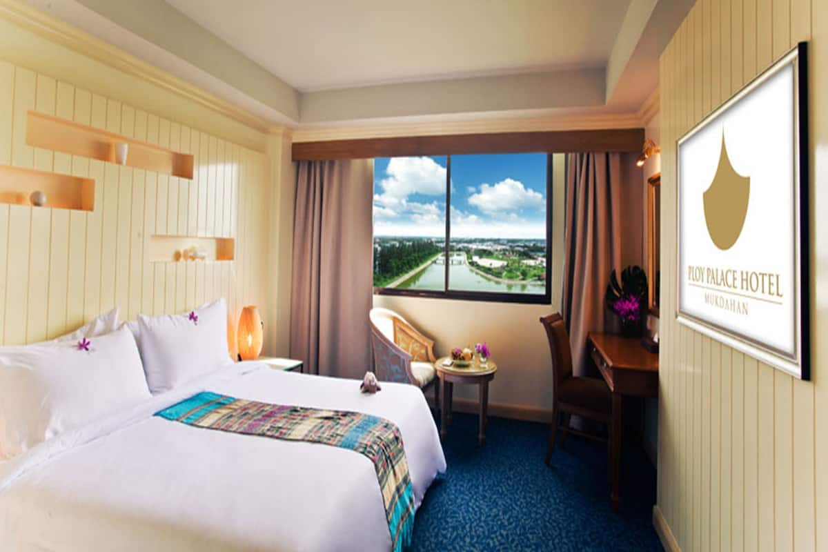 A hotel room with a large bed, a desk, a chair, and a view of a cityscape through a large window.