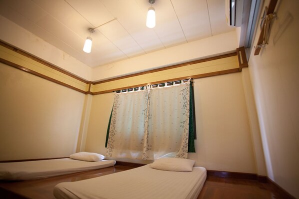 Una habitación con dos camas individuales, piso de madera, ventana con cortina floral y lámpara en el techo.