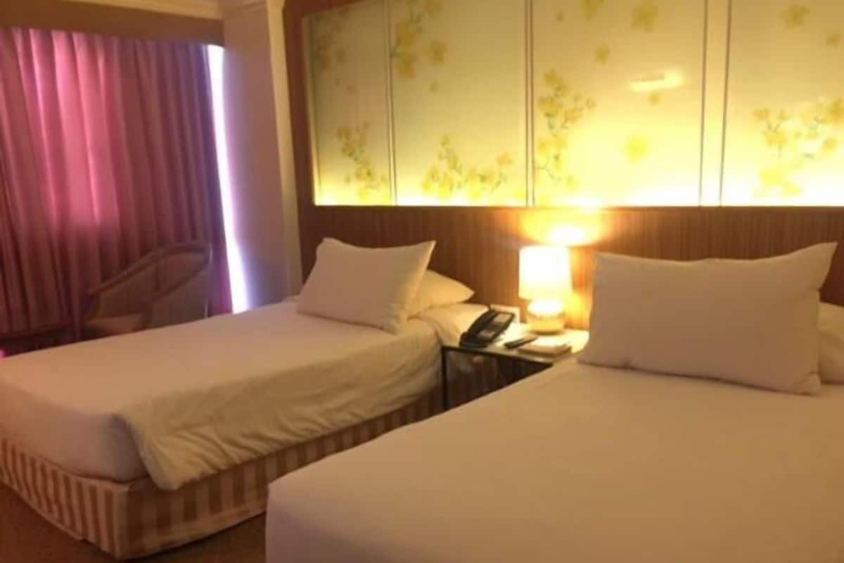 A hotel room with two beds, a chair, a nightstand with a lamp, and a floral wall panel.