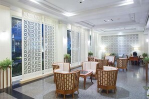 A lobby with a seating area featuring wicker chairs and tables, a patterned wall, and a decorative white partition. - Ploy Palace Hotel (Mukdahan)