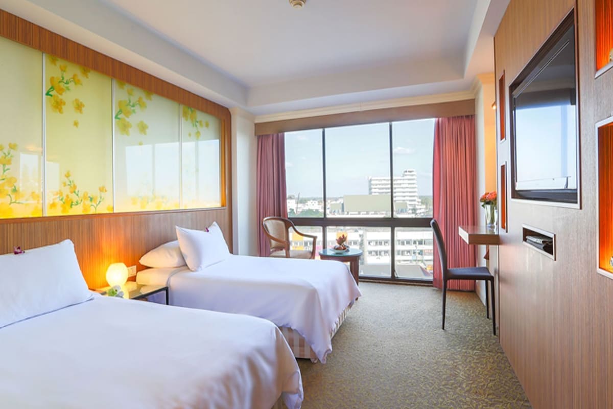 A hotel room with two beds, a desk, a chair, a TV, and a large window with a city view.