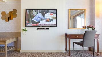 A room with a television mounted on the wall, a wooden desk, a chair, and a mirror.
