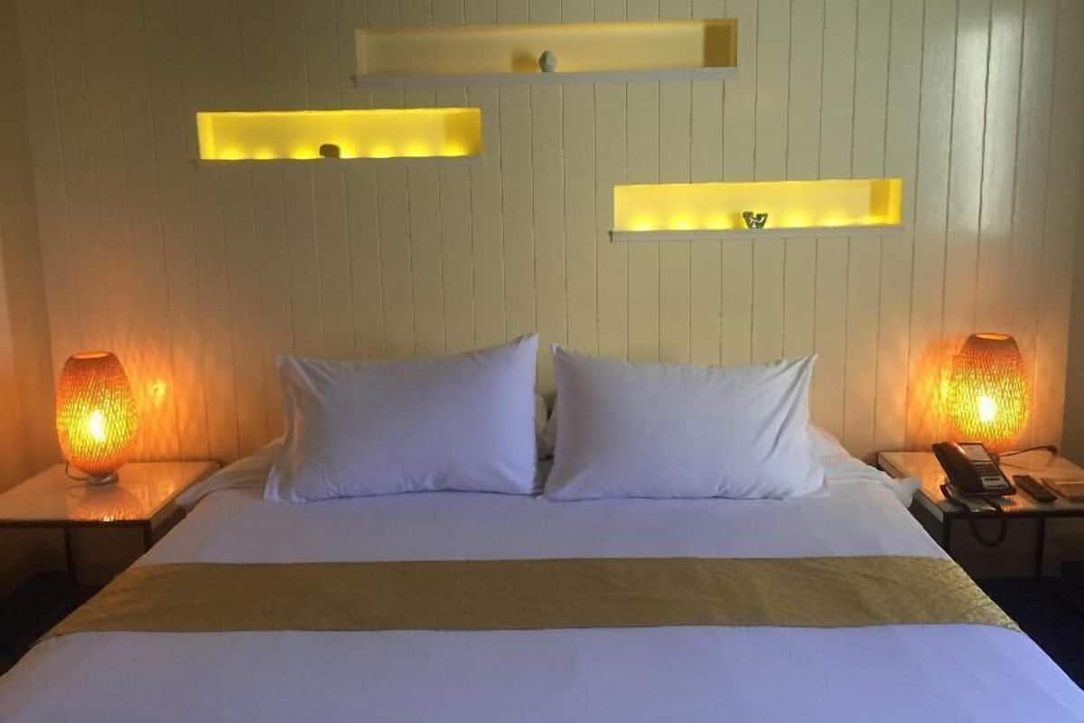 A hotel room with a bed, two bedside lamps, and three wall-mounted light fixtures.