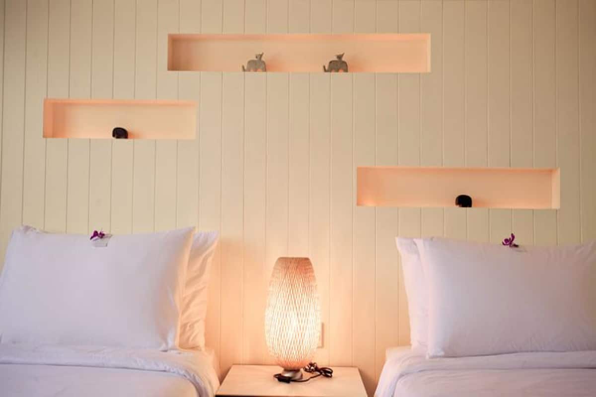 A hotel room with two beds, a nightstand with a lamp, and wall-mounted shelves with decorative items.