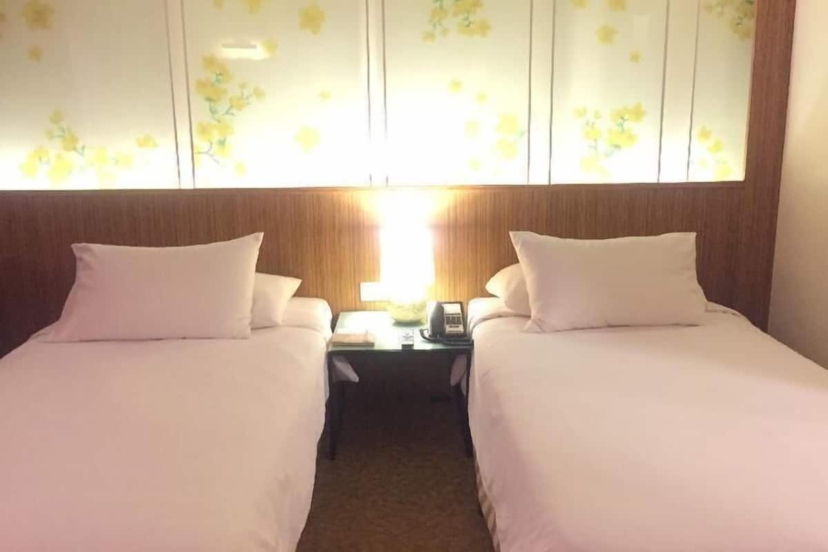 A hotel room with two beds, a wooden headboard, a nightstand with a phone, and a floral-patterned wall.