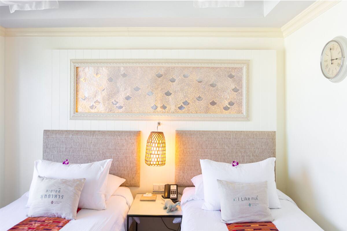 A hotel room with two beds, a nightstand, a lamp, a clock, and a decorative wall piece.