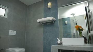 Un baño con inodoro, toallero, lavamanos con un jarrón de flores y zona de ducha.