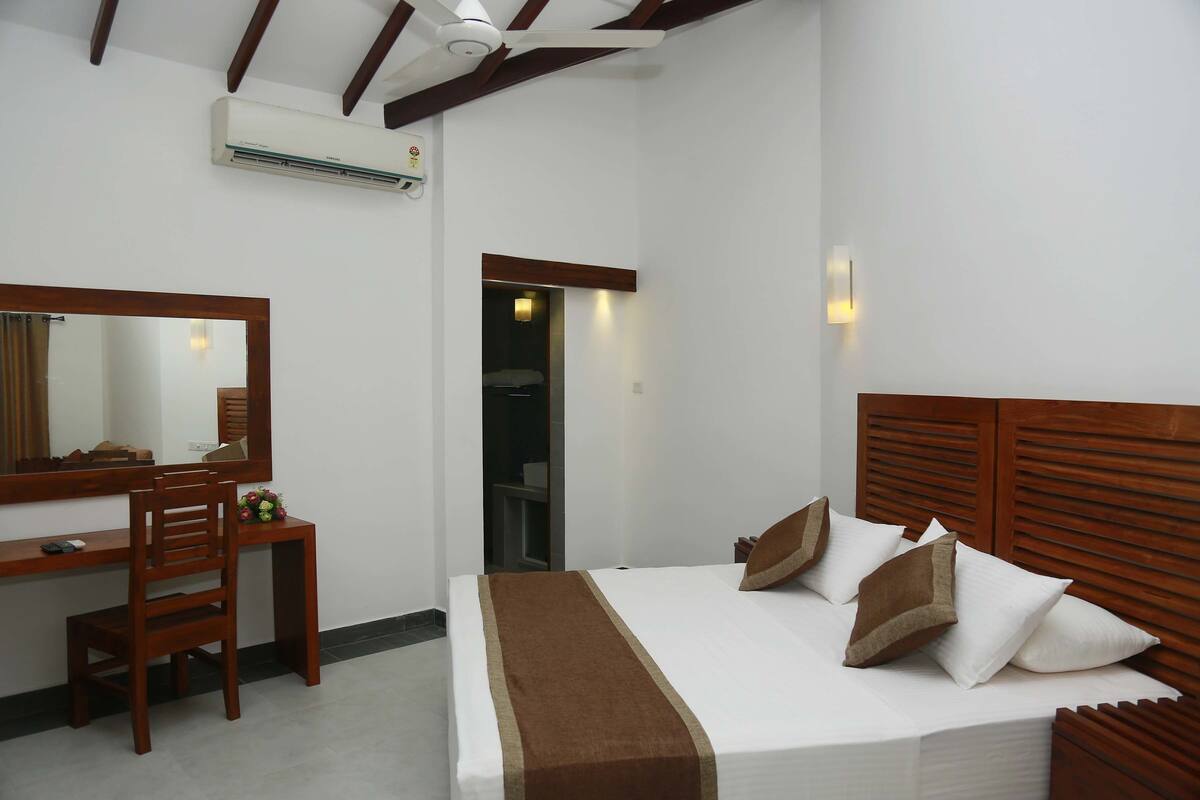 A bedroom with a bed, a desk, a chair, a mirror, and an air conditioning unit.