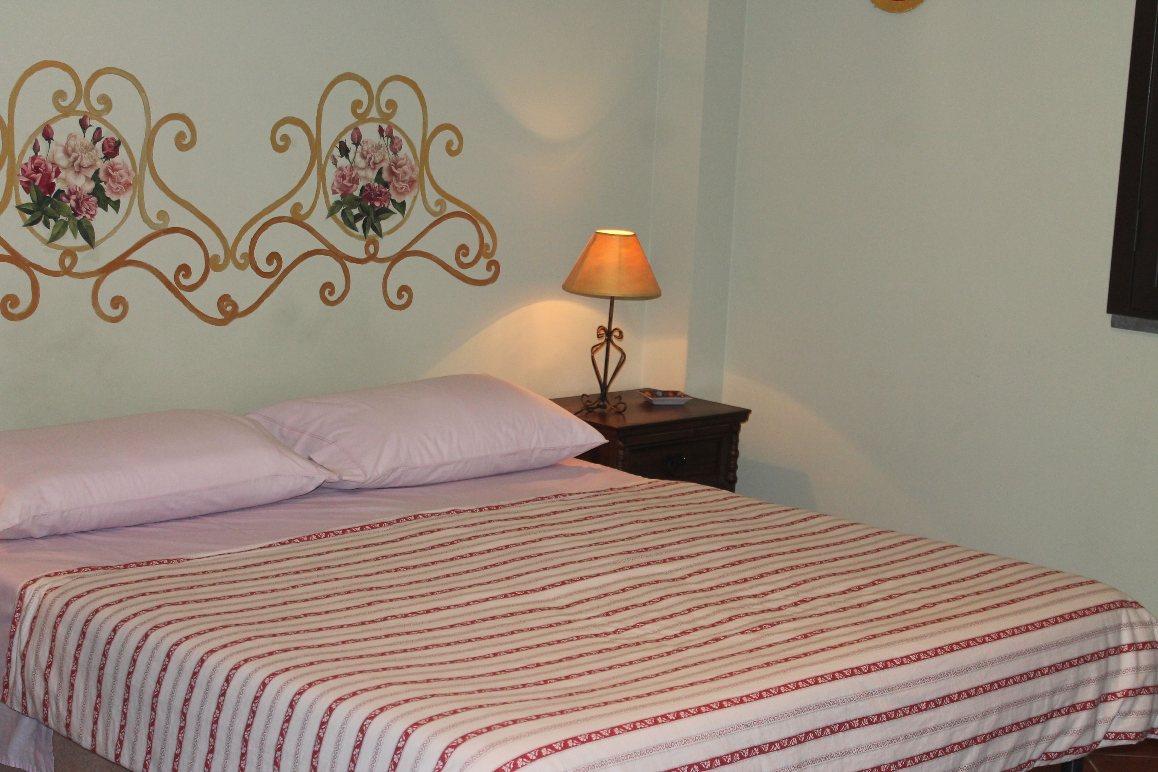 Un lit bien fait, recouvert d’une couvre-lit à rayures, une table de chevet avec une lampe et des œuvres d’art décoratives accrochées au mur au-dessus du lit.