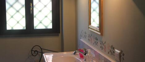 Une salle de bain avec un lavabo blanc, un miroir et une fenêtre dotée d’un store à motifs losangés.