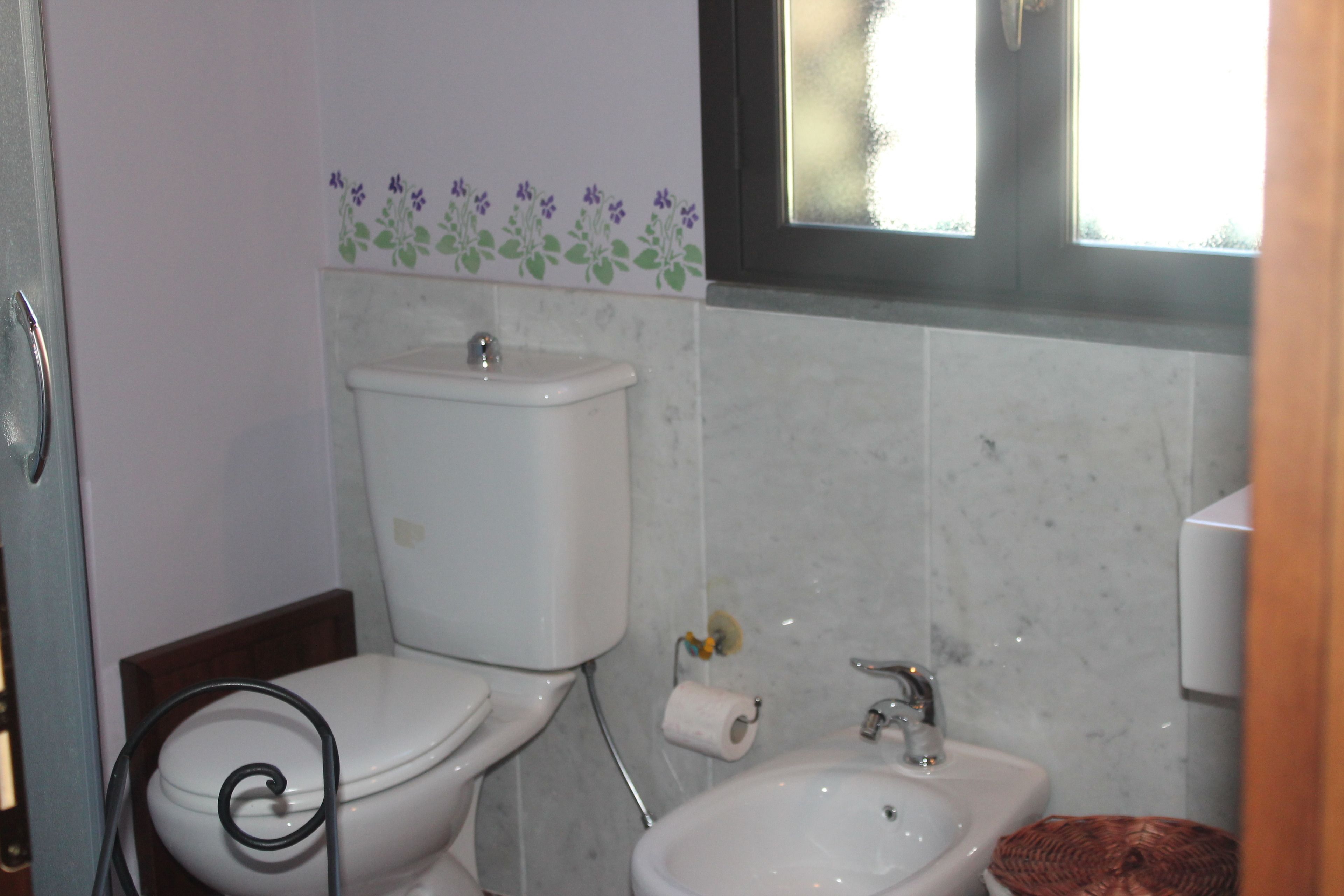 A bathroom with a toilet, sink, and a window.