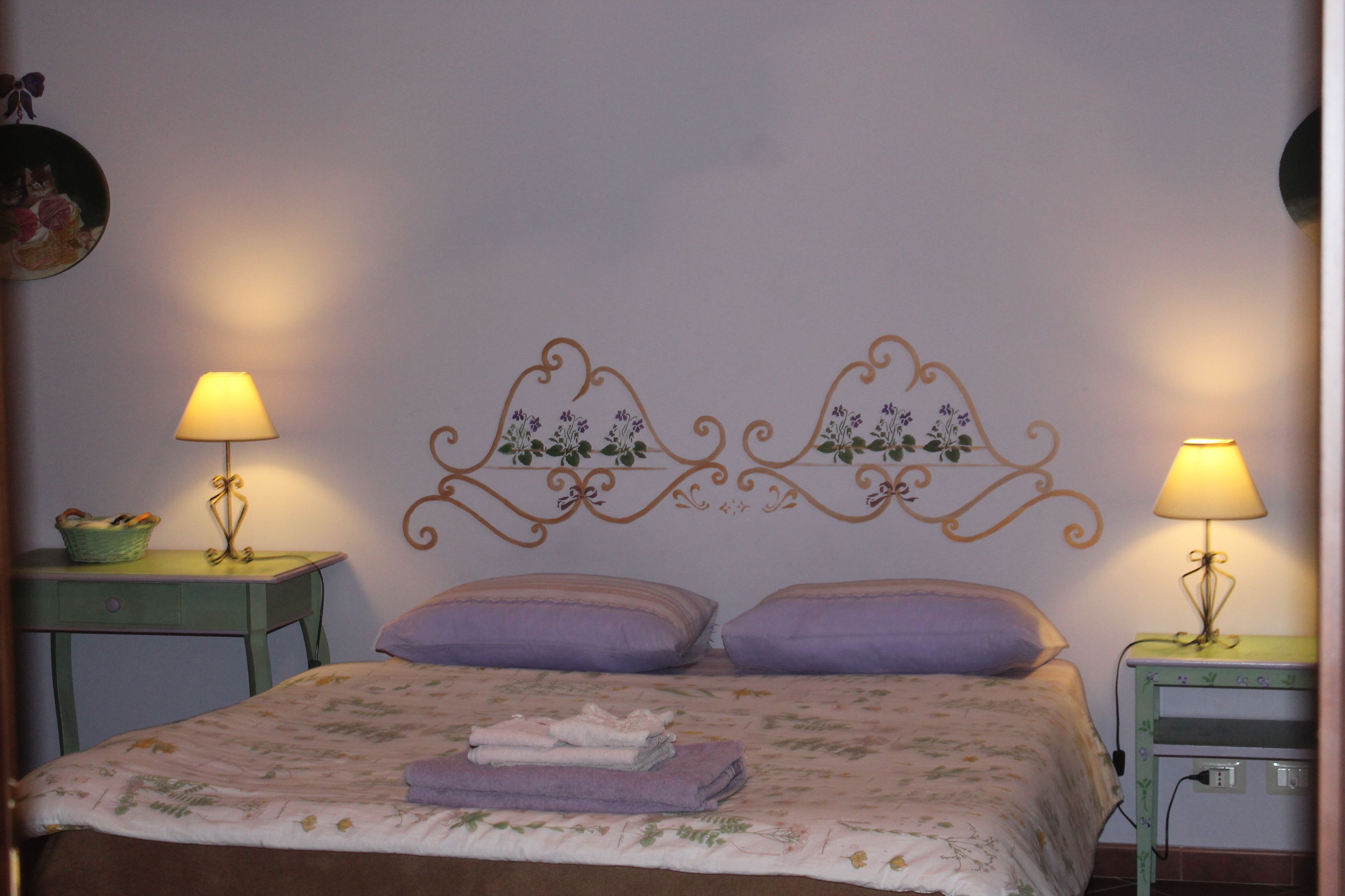 A neatly made bed with a floral bedspread and two pillows, flanked by two bedside tables with lamps and a decorative wall headboard.