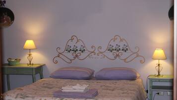 A neatly made bed with a floral bedspread and two pillows, flanked by two bedside tables with lamps and a decorative wall headboard.